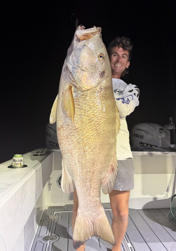Captain Noah Callais holding a large fish aboard a charter boat at night